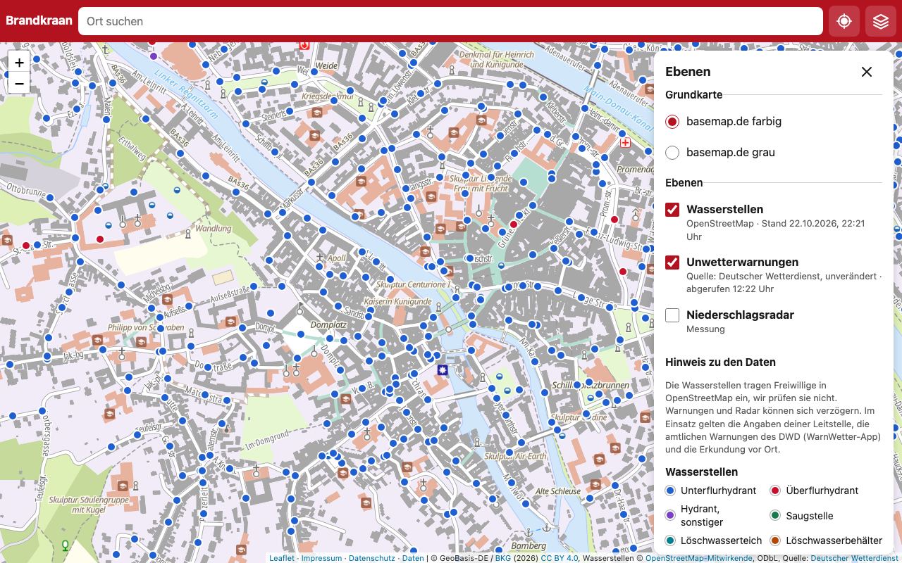 Die Karte am Computer: Altstadt von Bamberg auf der Grundkarte von basemap.de mit vielen farbigen Punkten für Unter- und Überflurhydranten, rechts die geöffnete Ebenenauswahl mit Wasserstellen, Unwetterwarnungen und Niederschlagsradar, darunter Datenhinweis und Legende.